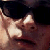 A pixelated close-up of a person's face with dark hair and a light-colored shirt against a dark background.