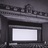 A pixelated grayscale image shows a dark rectangular frame with a bright white rectangle inside, set against a textured background with horizontal bands and scattered darker shapes.