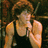 Pixelated image of a person with light brown hair wearing a black sleeveless top, holding hands near the face against a dark background.