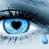 A close-up of a human eye with blue irises, a black heart-shaped pupil, and a single blue teardrop falling from the lower right corner.