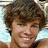 Pixelated close-up of a person with curly brown hair, light skin tone, and visible facial features including eyes, nose, mouth, and chin.