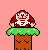 Pixelated character with brown hair and white face on green ring atop brown column against pink background.