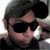 A person wearing dark sunglasses and a dark cap, with a hand near their face, shown in a of with slight variations in pose and lighting