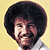 Pixelated static image of a person with an afro hairstyle against a yellow background, wearing a light-colored shirt.