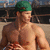 A pixelated image of a shirtless person wearing a green cap, standing in front of an indistinct background with dark and light tones.