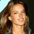A pixelated close-up of a person with long brown hair, light skin, and a neutral expression against a light blue and dark background.