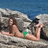 A pixelated image of a woman in a green bikini lying on rocks by the sea, with blue text reading "TELL ME WHY I LOST U" and partial phrases below.