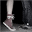Pixelated image of two people's legs and feet, one wearing brown shoes with white laces and white socks, the other in dark pants and white sneakers, next to red text reading "My Heart Won't Stop Screaming" on black background.