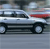 Pixelated static image of a silver sedan with black trim and red accents on the roof, viewed from a low angle on a gray road surface.