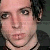 Pixelated close-up of a person's face with light skin tone, dark hair, and visible neck, wearing a dark top with a thin strap.
