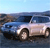 Pixelated image of a light-colored convertible car with dark roof, positioned on a road against a blue sky and distant landscape.