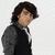 A pixelated image of a person with dark hair wearing a dark vest over a light shirt against a light background.