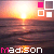 Sunset over water with a of four squares in top-left corner; text 'Madison' appears below the scene