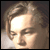 Pixelated static image of a person's face with light brown hair and closed eyes, rendered in warm tones on a dark background.