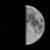 A pixelated grayscale crescent moon shape against a solid black background, with visible texture variations across its surface.