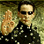 Pixelated image of a person wearing dark sunglasses and a black shirt with white speckles, holding up a hand in a waving gesture against a greenish background.