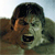 Pixelated close-up of a person with dark hair and light skin, mouth open in a shout or yell, against a blurred outdoor background.