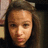 Pixelated close-up of a person with light brown hair and fair skin, wearing dark clothing against a dimly lit background.