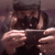 A person wearing a dark cap and shirt holds a small device horizontally with both hands, positioned close to their face.