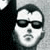 Pixelated grayscale image of a person's face wearing dark sunglasses, with a dark shape on the left side of the frame.