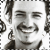 Black-and-white portrait of a smiling person with long hair, wearing earrings and dark clothing, framed by dashed borders.