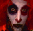 Pixelated static image of a stylized face with dark eye sockets, red background, and visible dithering artifacts.