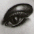 A dark, pixelated oval-shaped icon with a glossy highlight on the top right and subtle internal shading against a light gray background.