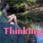 A pixelated image of a person with long hair holding their head, overlaid with pink text reading Thinking about him.