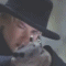 A woman with blonde hair and a black hat holds a smoking pistol, then the smoke clears to reveal her face in a sequence of frames.