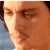Pixelated close-up of a person's face with light skin tone, brown eyes, and dark hair, wearing a light-colored shirt against a blurred background.