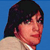 Pixelated static image of a person with dark hair and light skin against solid blue background, cropped to show upper shoulders and head in profile view.