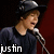 A person in a dark hat and shirt sings into a microphone with a red background, showing text variations and a heart symbol.