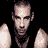 Pixelated static image of a bald man with dark hair on sides, wearing black sunglasses and a black sleeveless shirt against solid black background.