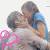 Pixelated static image of two figures in close embrace with indistinct facial features and blurred colors, featuring pink floral elements on the left side against a light background.