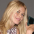 A static pixelated image shows a person with long blonde hair holding a dark blue object near their face against a gray background.