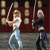 Two pixelated figures holding swords in front of a wall of framed pictures, one in light clothing, the other in dark clothing.