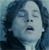 Pixelated close-up of a person with dark curly hair, closed eyes, and an open mouth against a blue gradient background.