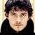 Pixelated static image of a person with dark hair and light skin wearing a black top against a beige background.