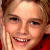 A pixelated close-up of a person with light skin, brown hair, and dark eyes smiling broadly while resting their right hand against their cheek.