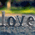 A four- shows a stone monument with 'love' carved in water, two figures holding hands under a heart symbol, and a handwritten note reading 'P.S. I LOVE U'