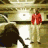 Animated sequence showing a figure in red clothing moving through a stone archway and interacting with a seated figure in a dark interior space.
