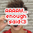 A pixelated image of a person with brown hair wearing red clothing, holding hands near their head against a light gray brick background.
