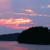 Pixelated landscape showing a dark silhouette of landmass against a gradient sky with pink and orange clouds at dusk.