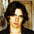 Pixelated static image of a person with dark shoulder-length hair, light skin, and a neutral expression against a textured background.