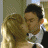 A pixelated image shows two people in close physical proximity, one with light brown hair and the other with dark hair, both wearing light-colored clothing against a muted background.