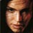 Pixelated static image of a person's face with warm skin tones and dark hair, cropped to show eyes, nose, mouth, and forehead against a dark background.