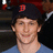 Pixelated static image of a person with short dark hair wearing a dark cap with red emblem and light blue shirt against dark background.