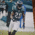 Pixelated static image of a football player in dark uniform with blue accents holding a ball, standing on grassy field near white goalpost.