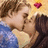 Two figures in close proximity with one figure's hand near the other's face, a pink heart symbol in the upper right, and a pixelated background.