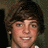 Pixelated close-up of a person with dark brown hair, light skin, and a white shirt collar visible at the bottom edge.